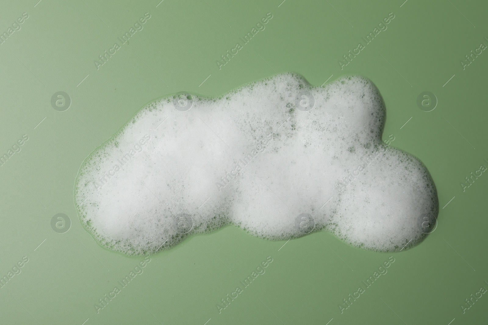 Photo of Drop of fluffy soap foam on green background, top view