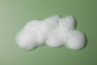 Drop of fluffy soap foam on green background, top view