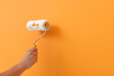 Photo of Worker using roller to paint wall with orange dye, closeup