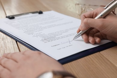 Photo of Woman signing contract at wooden table, closeup.