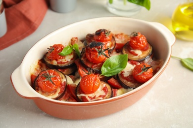 Baked eggplant with tomatoes, cheese and basil in dishware on light table, closeup