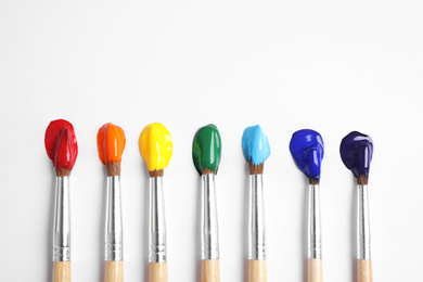 Photo of Brushes with bright paints on white background, flat lay. Rainbow colors