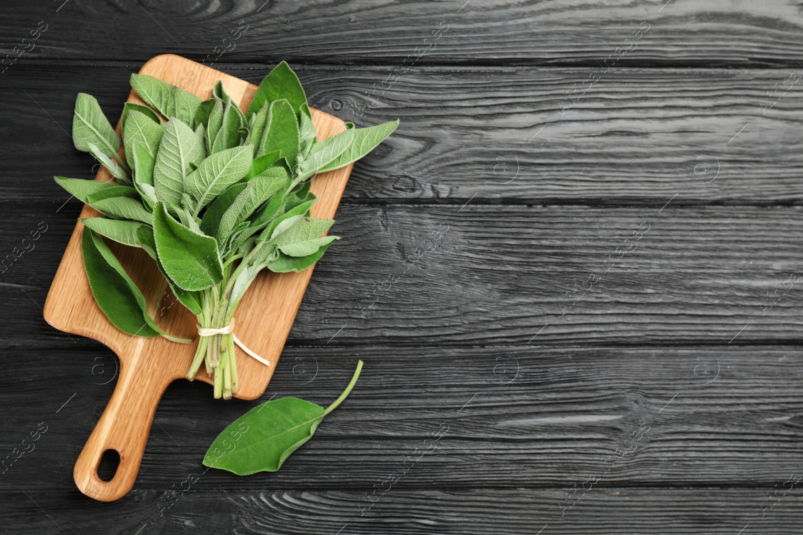 Photo of Bunch of fresh sage leaves on black wooden table, flat lay. Space for text