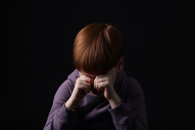 Sad little boy crying on black background