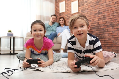 Photo of Cute children playing video games while parents resting on sofa at home
