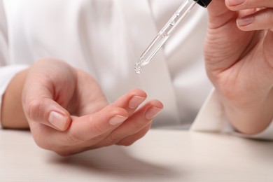 Photo of Woman applying cosmetic serum onto finger at white table, closeup