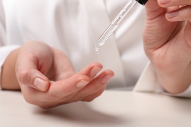 Woman applying cosmetic serum onto finger at white table, closeup