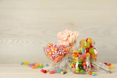 Photo of Jars with different delicious candies on beige wooden table, space for text