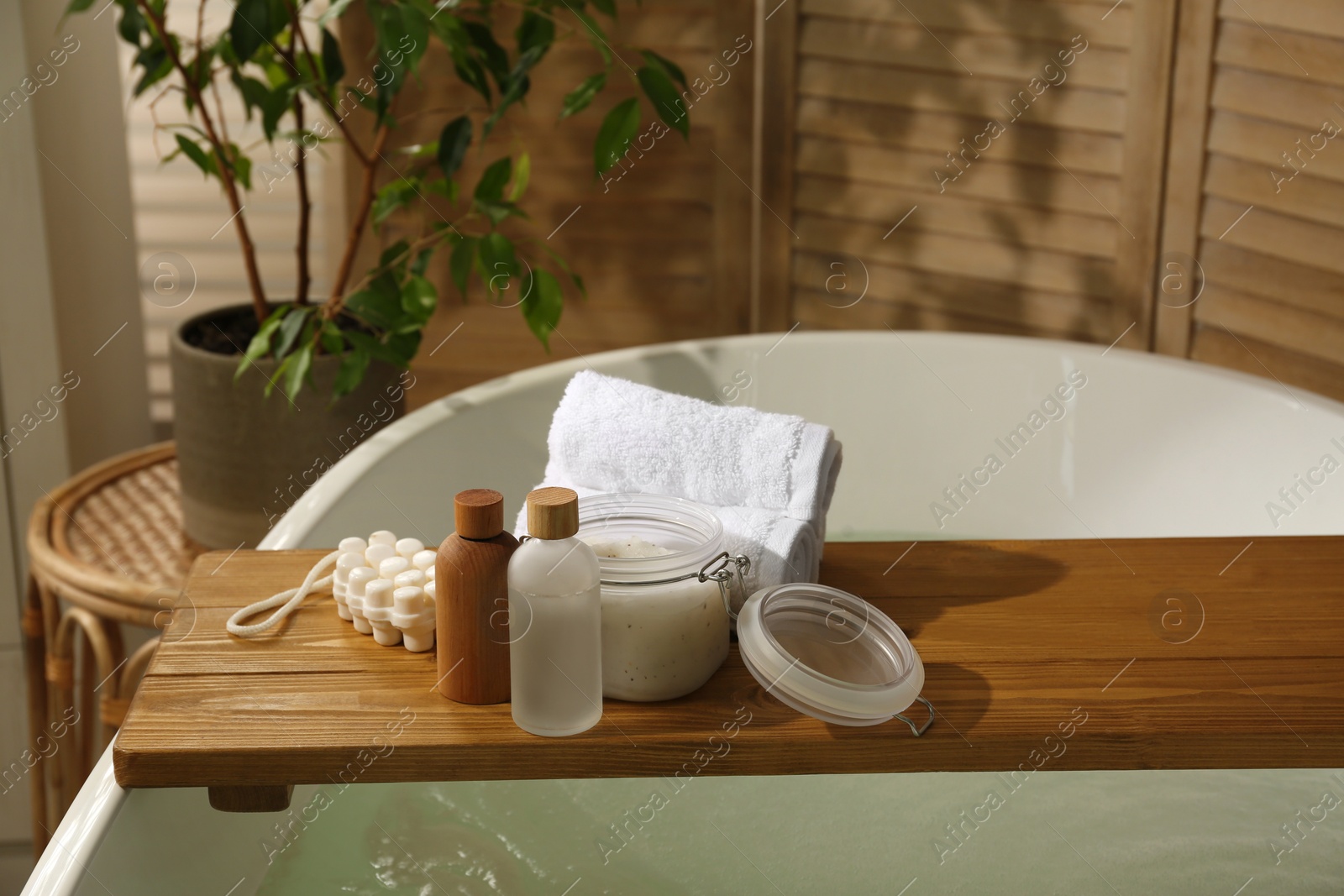 Photo of Wooden tray with spa products and towels on bath tub in bathroom. Space for text