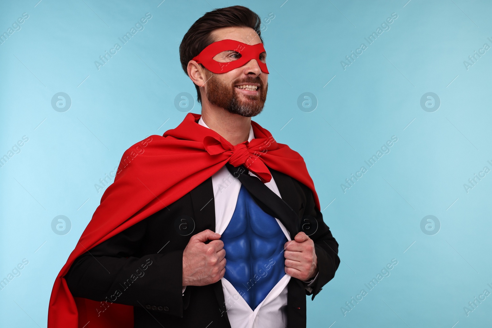 Image of Happy businessman wearing superhero costume under suit on light blue background