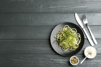 Photo of Delicious zucchini pasta with arugula, pumpkin seeds and sauce served on grey wooden table, flat lay. Space for text