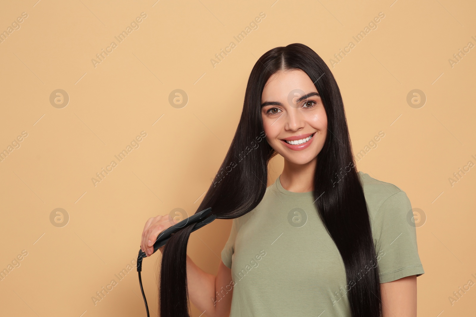 Photo of Beautiful happy woman using hair iron on beige background. Space for text