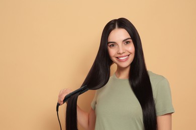 Beautiful happy woman using hair iron on beige background. Space for text