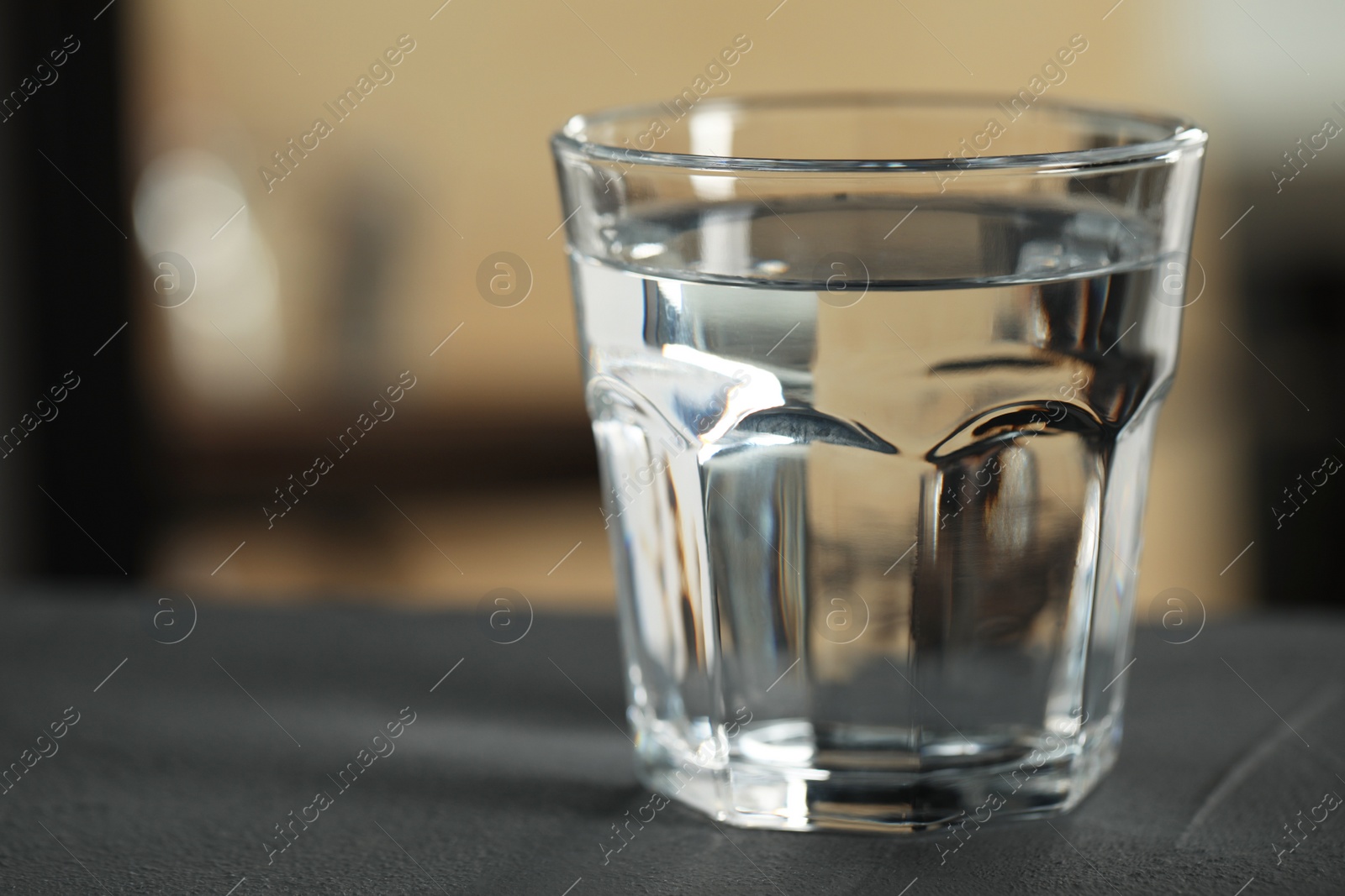 Photo of Glass of pure water on black table against blurred background, space for text