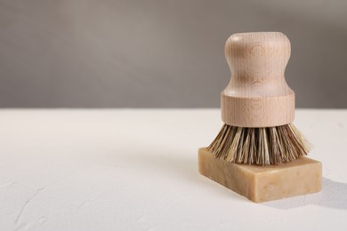 One cleaning brush and bar of soap on white textured table, closeup. Space for text