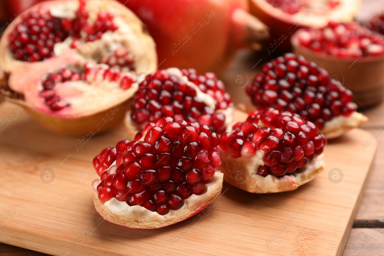 Photo of Delicious ripe pomegranates on wooden board, closeup