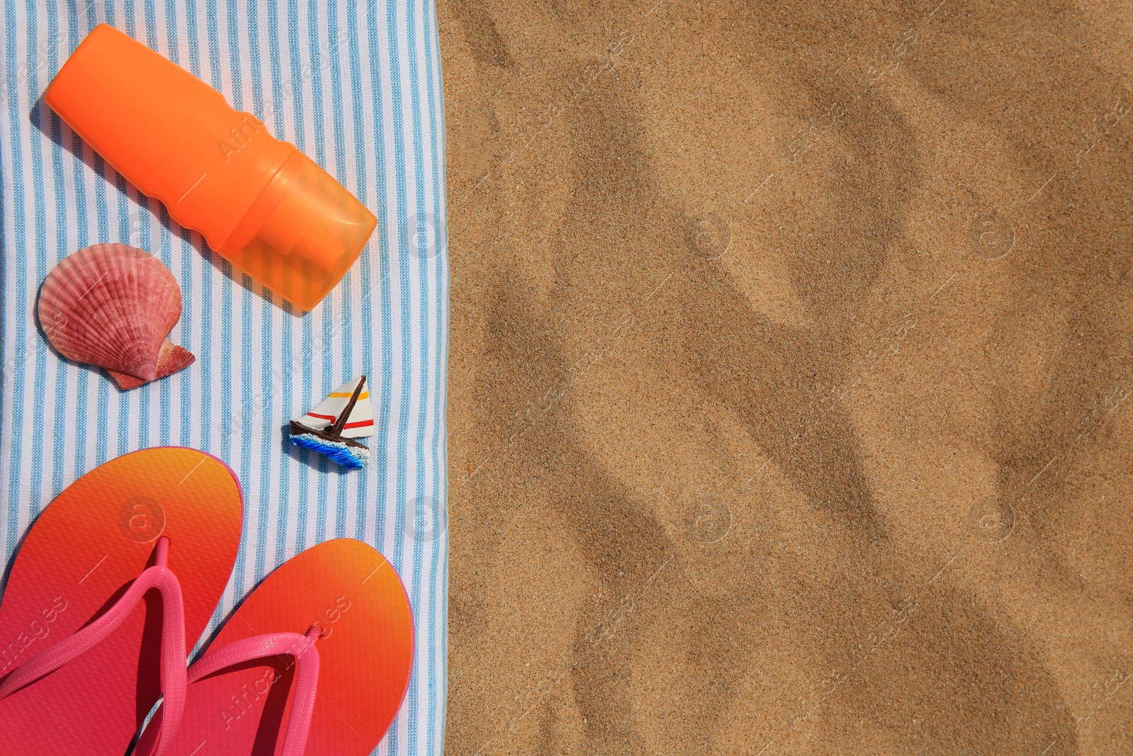 Photo of Bottle of sunscreen, flip flops and towel on sand, top view with space for text. Sun protection care