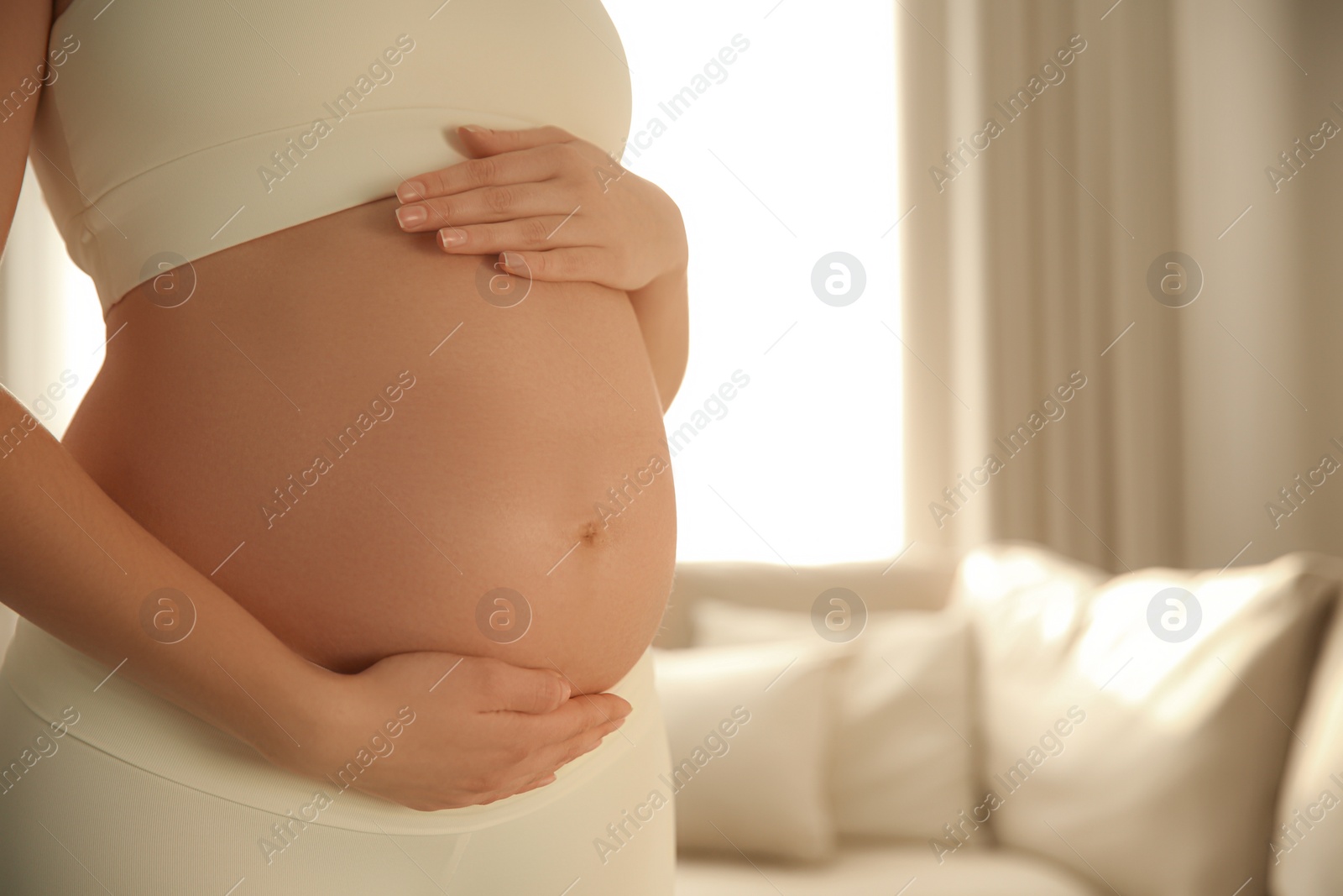 Photo of Pregnant woman touching her belly indoors, closeup