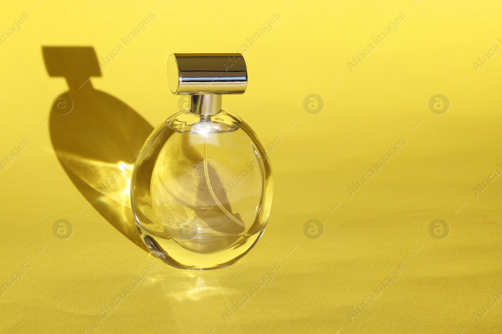 Photo of Luxury women's perfume. Sunlit glass bottle on yellow background. Space for text