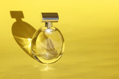 Luxury women's perfume. Sunlit glass bottle on yellow background. Space for text