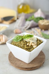 Photo of Bowl with delicious pesto sauce, cheese, pine nuts and basil leaves on light table, closeup