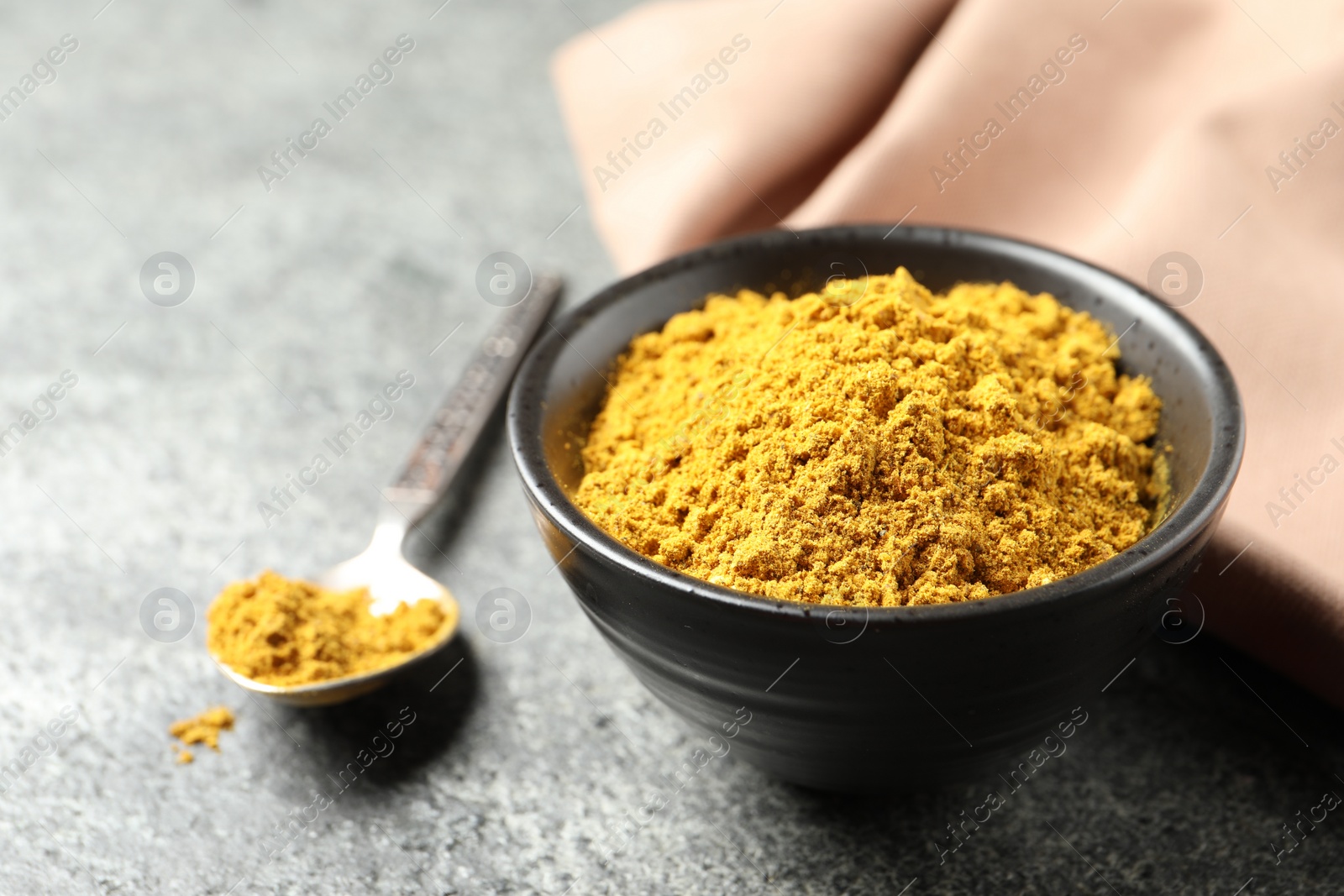 Photo of Dry curry powder in bowl and spoon on dark table, closeup