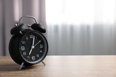 Black alarm clock on wooden table indoors, space for text