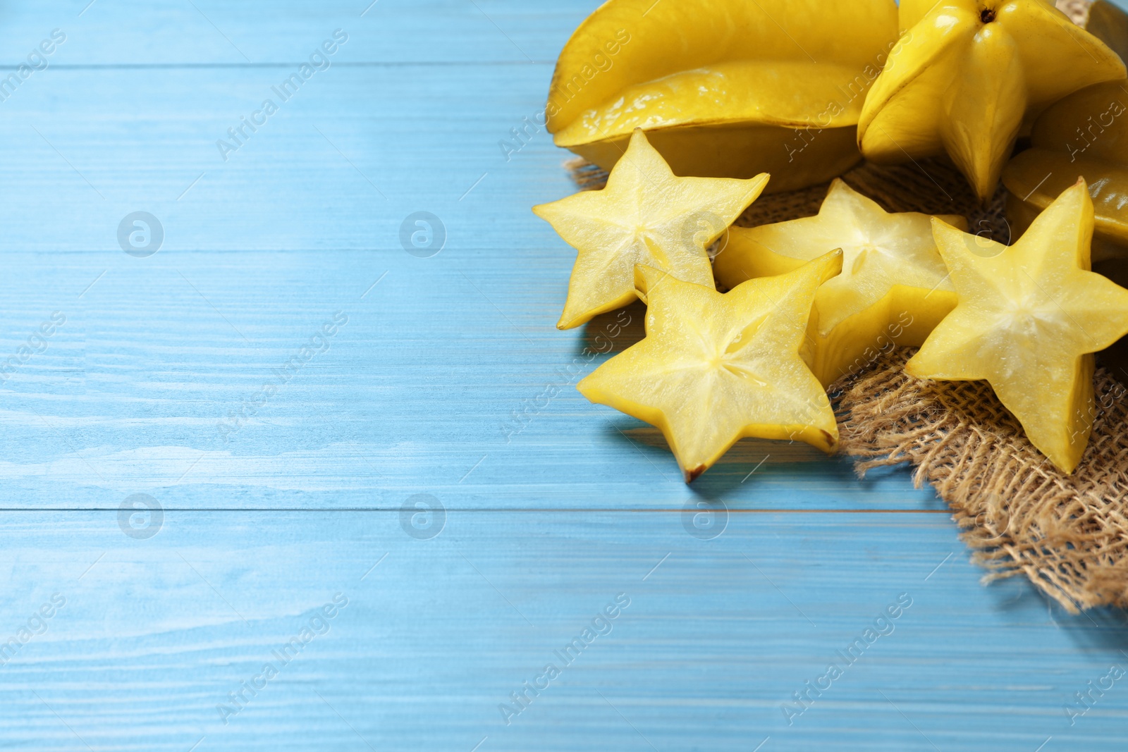 Photo of Cut and whole carambolas on turquoise wooden table. Space for text