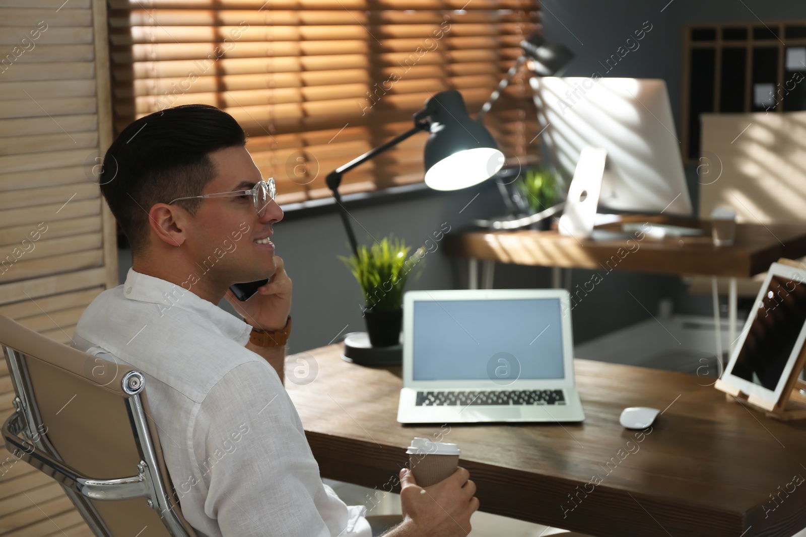 Photo of Freelancer with cup of coffee talking on phone while working indoors