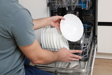 Man loading dishwasher with plates indoors, closeup