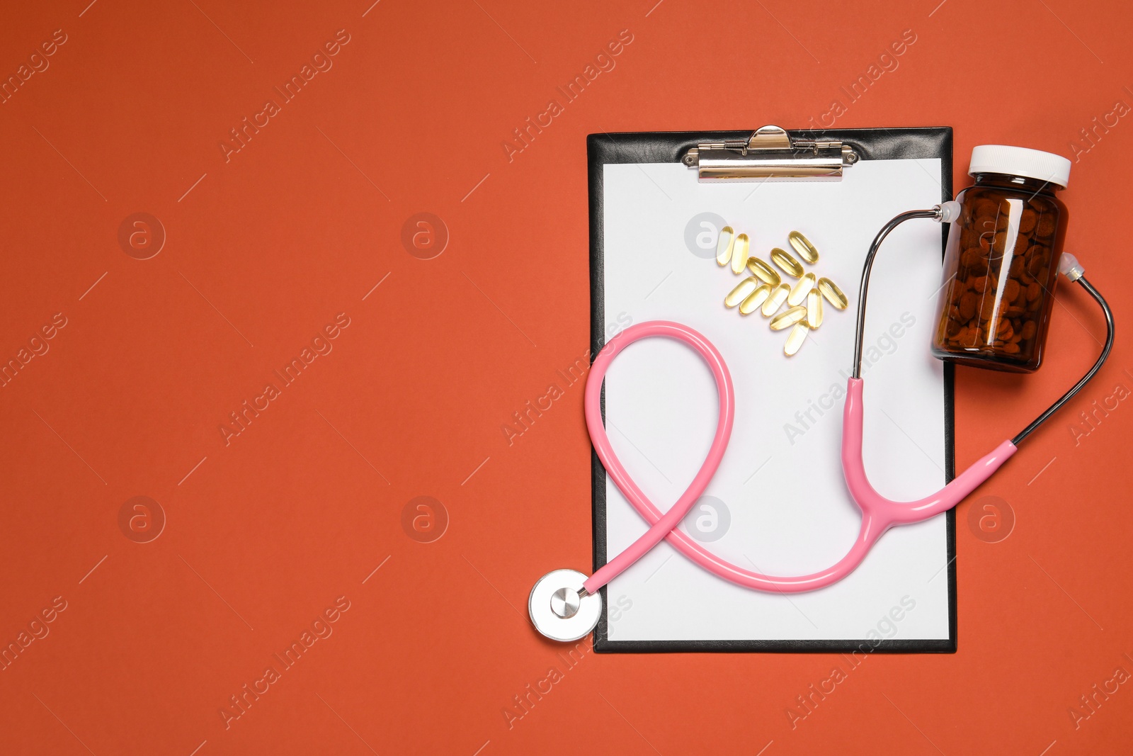 Photo of Stethoscope, pills and clipboard on crimson background, flat lay. Space for text