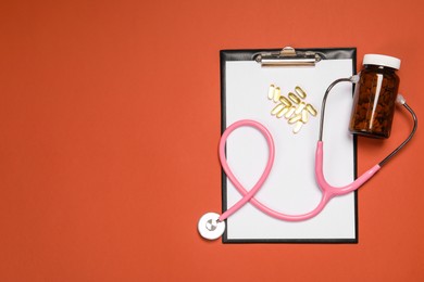 Photo of Stethoscope, pills and clipboard on crimson background, flat lay. Space for text