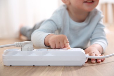 Photo of Little child playing with power strip on floor indoors, closeup. Dangerous situation