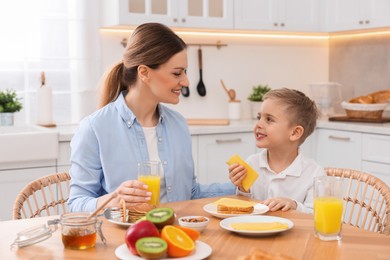 Mother and her cute little son having breakfast at table in kitchen