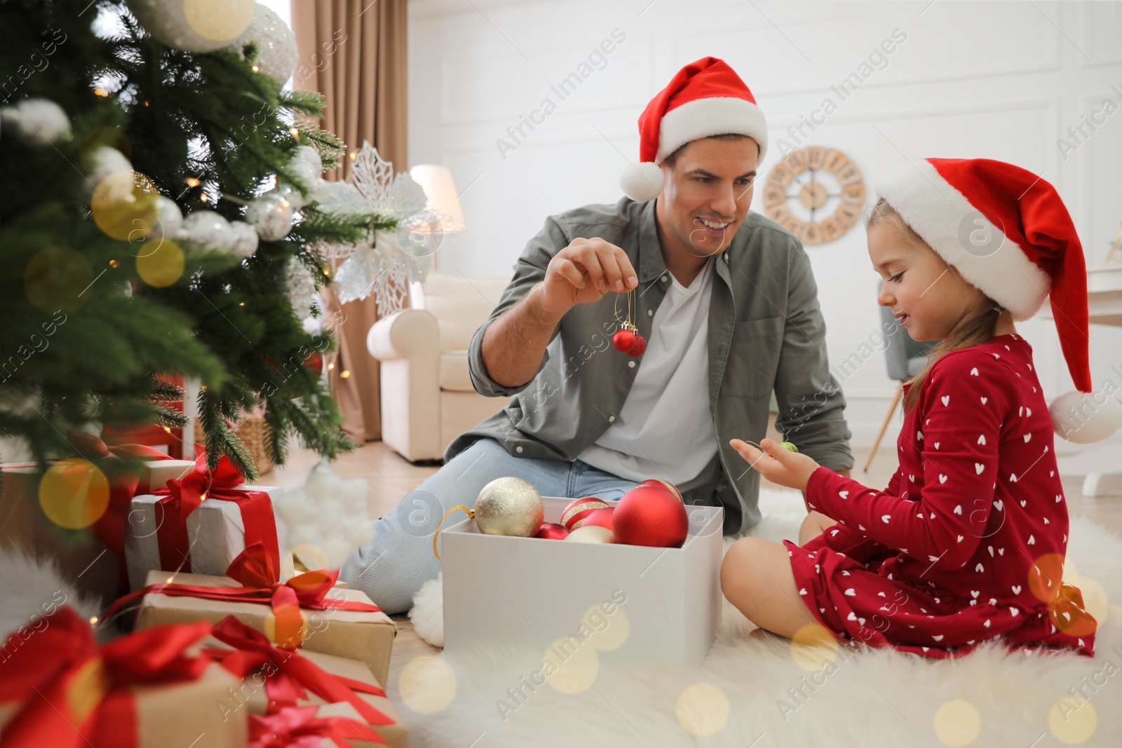 Photo of Father with his cute daughter in Santa hats decorating Christmas tree together at home