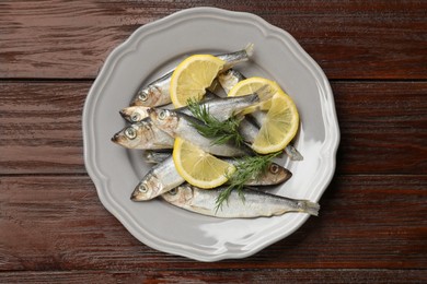 Fresh raw sprats, dill and cut lemon on wooden table, top view