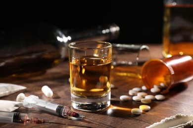 Photo of Alcohol and drug addiction. Whiskey in glass, syringes, pills and cocaine on wooden table