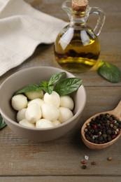 Photo of Tasty mozarella balls, basil leaves and spices on wooden table