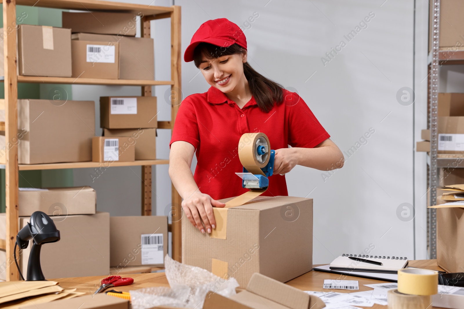 Photo of Parcel packing. Post office worker taping box at wooden table indoors