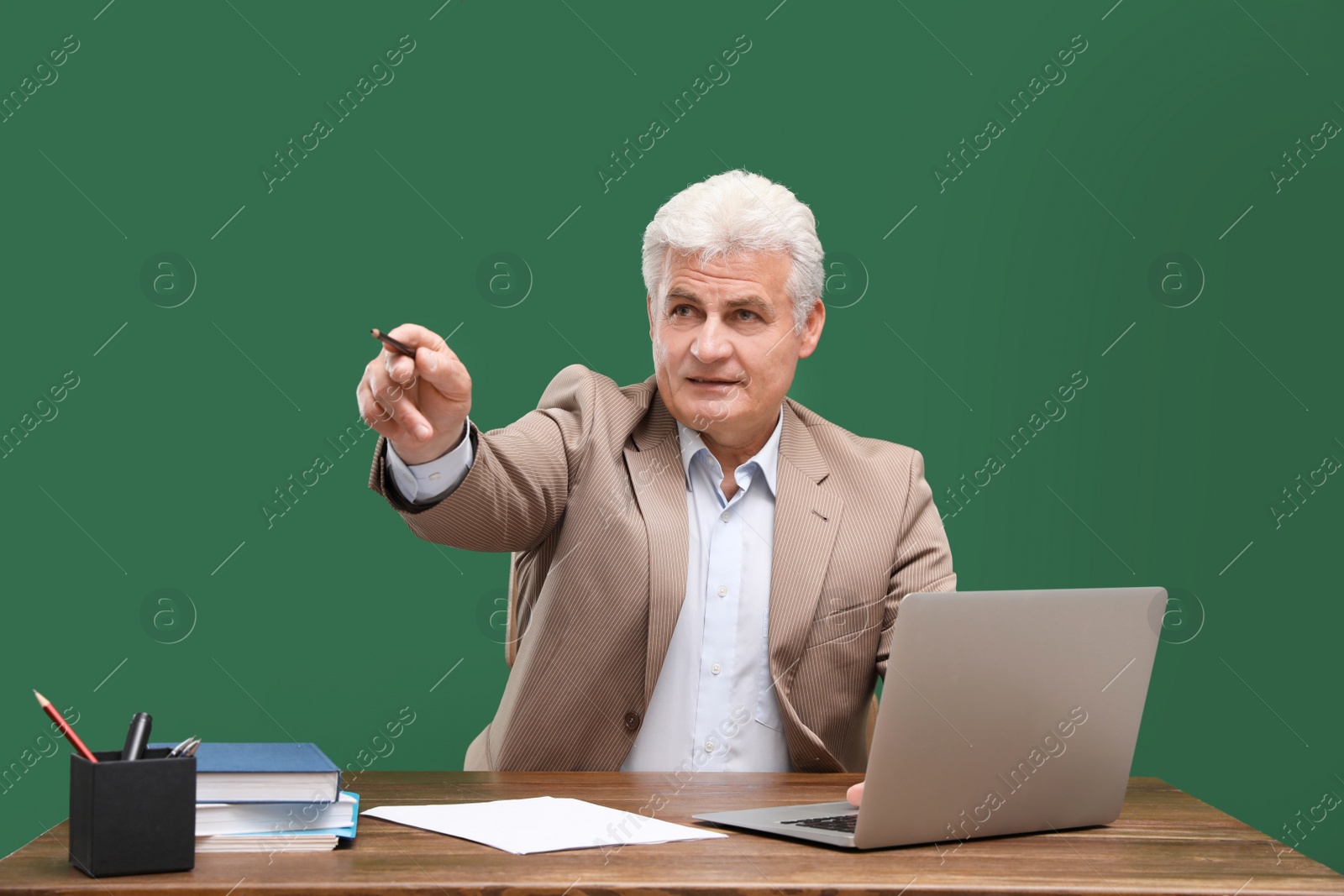 Photo of Portrait of senior teacher with laptop at table against green chalkboard