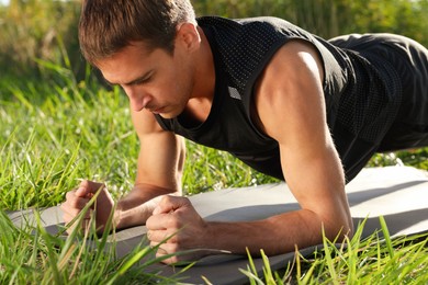 Sporty man doing plank exercise on green grass