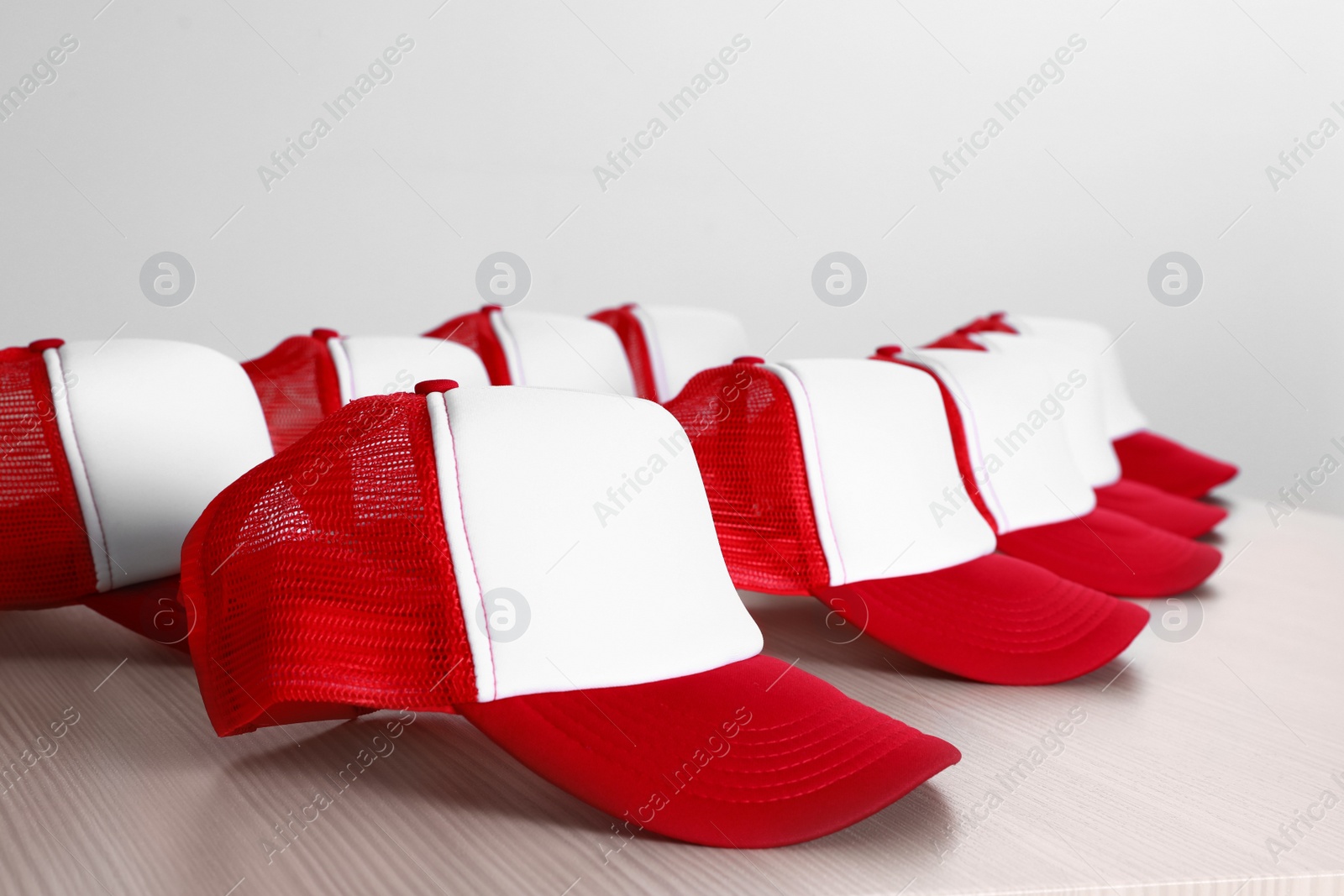 Photo of Many blank colorful caps on wooden table near light wall. Mock up for design