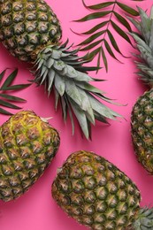 Photo of Whole ripe pineapples and green leaves on pink background, flat lay