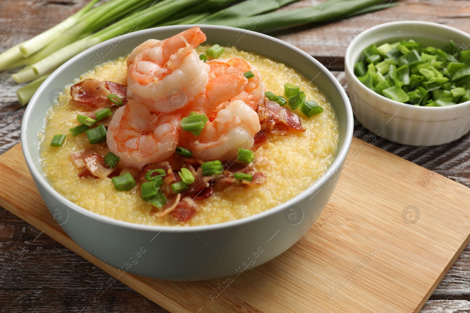 Photo of Fresh tasty shrimps, bacon, grits and green onion in bowl on wooden table, closeup