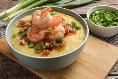 Photo of Fresh tasty shrimps, bacon, grits and green onion in bowl on wooden table, closeup