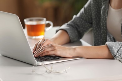 Woman working with laptop at white table indoors, closeup