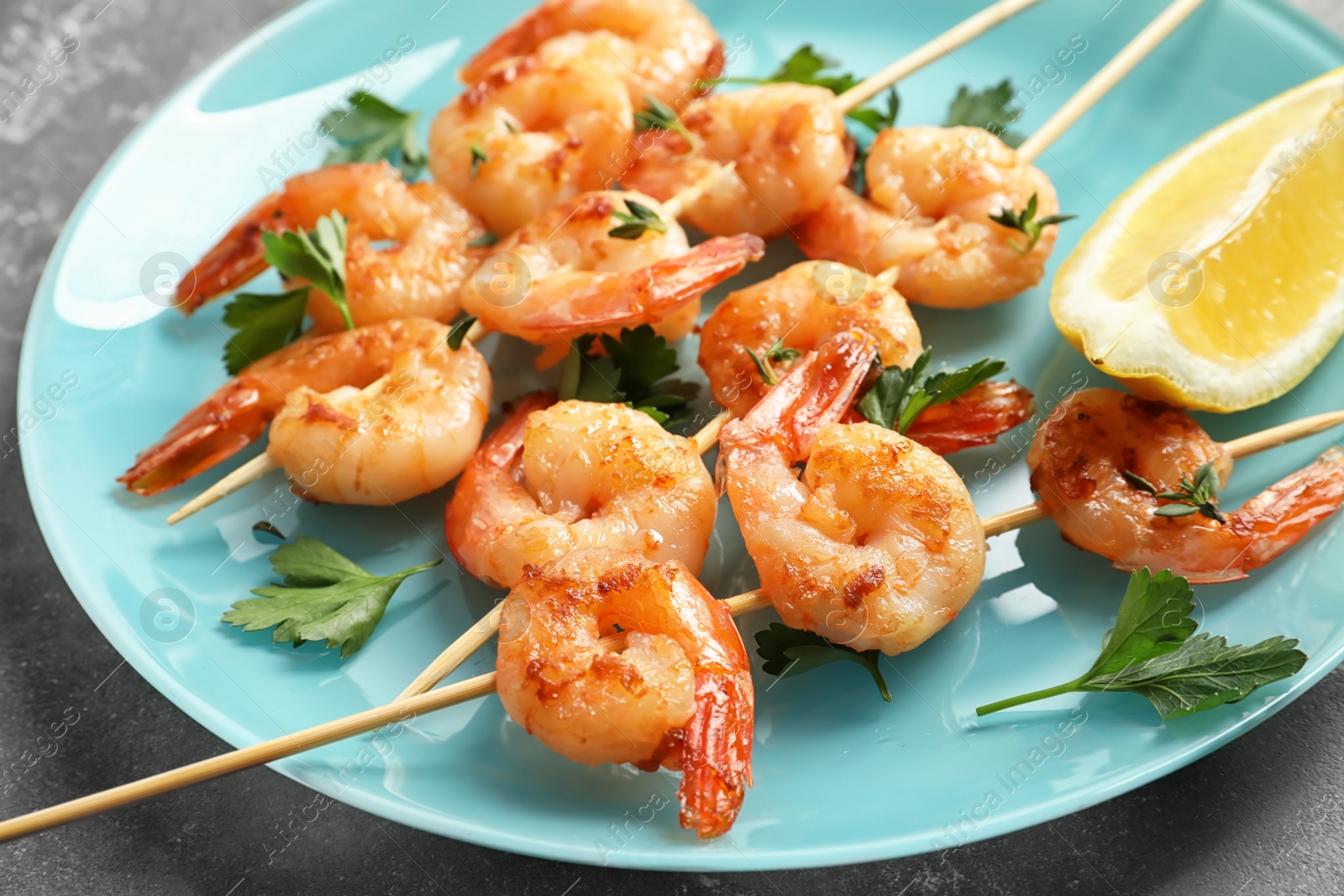 Photo of Plate with delicious fried shrimp skewers and lemon on grey background, closeup