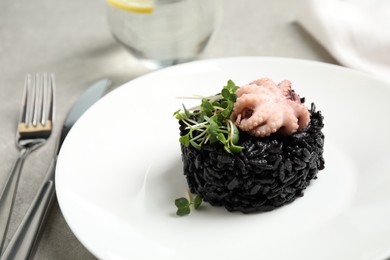 Photo of Delicious black risotto with baby octopus on light table, closeup