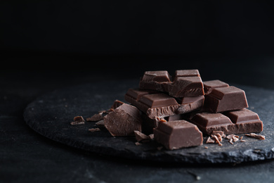 Photo of Pieces of delicious natural milk chocolate on slate plate
