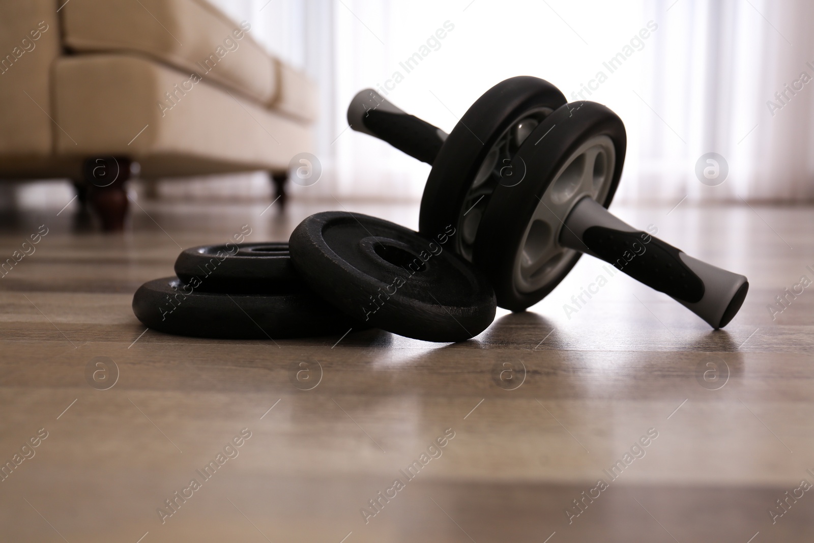 Photo of Abs roller and weight plates on floor in room. Home fitness